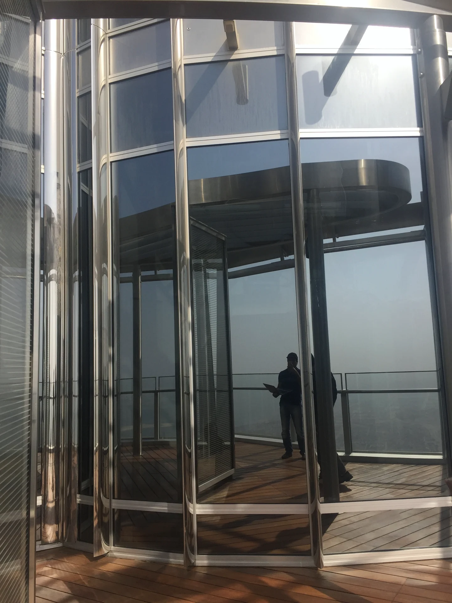 Curved glazed enclosure with stainless-steel framing, timber decking and people visible through the glass.