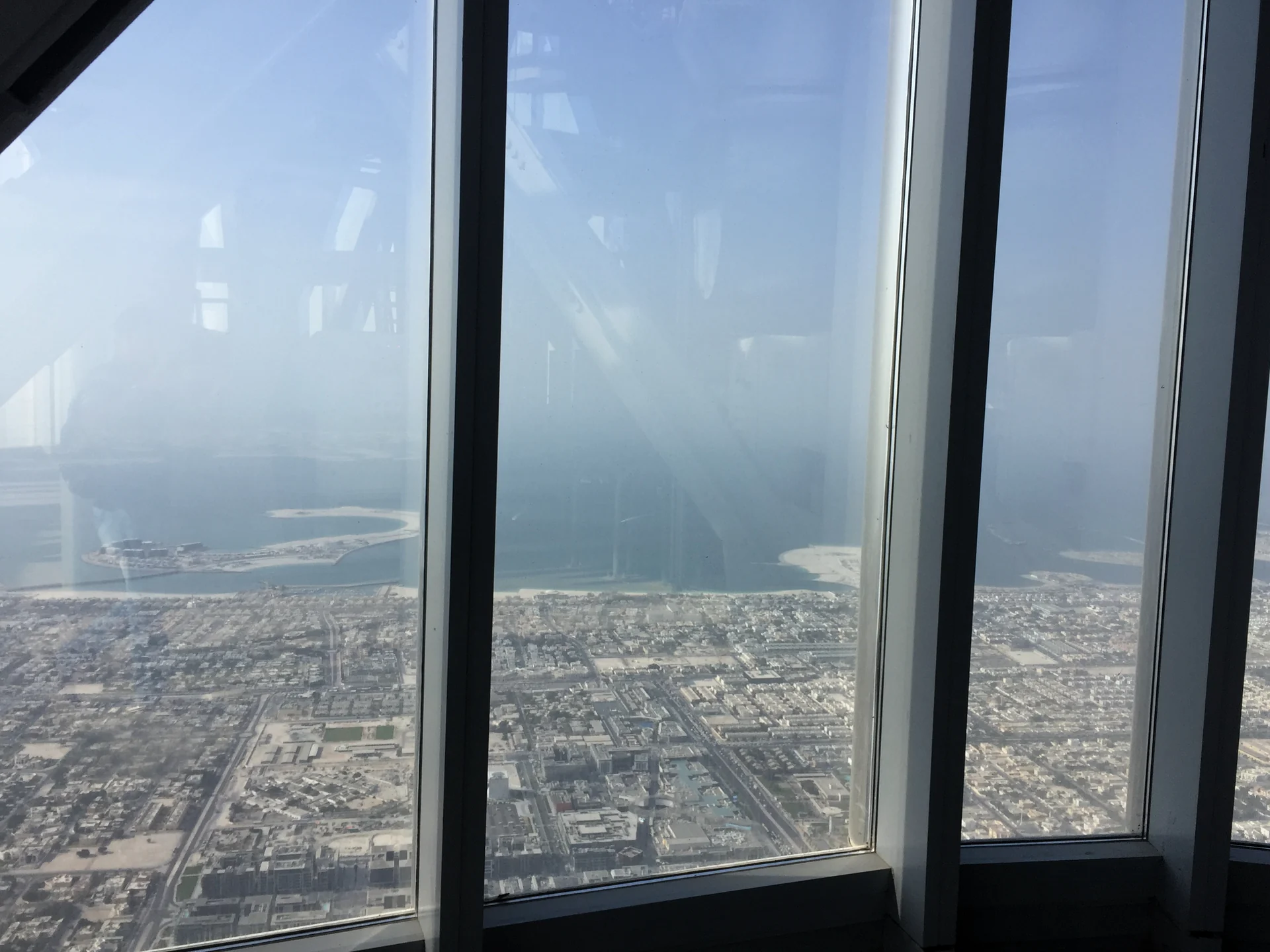 City and coastal view through high-rise glazing, with mullions and interior reflections visible.